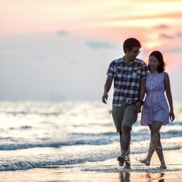 Couple walking along beach hand in hand at sunset